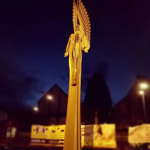 Eine hohe, gelbe Engelsfigur mit Flügeln in Bargoed bei Nacht.