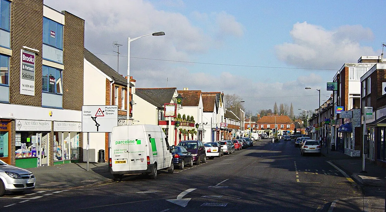 Blick auf Frimley High Street mit Geschäften und geparkten Autos.