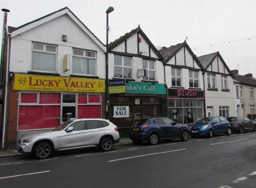 Geschäfte und geparkte Autos in einer Straße in Ystrad Mynach.