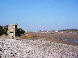 Stone tower on the beach with the harbour and causeway in the background.