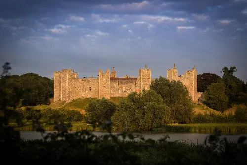 Castle with stone walls and towers at sunset, partly cloudy sky in the background.