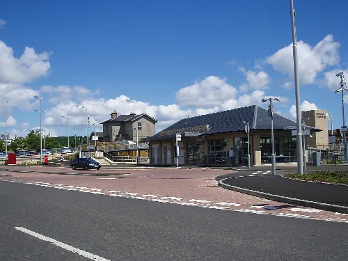 A modern train station with a parking area and old station building in the background.
