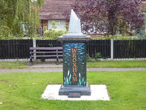 Stone village sign with boat and reeds design in a park.