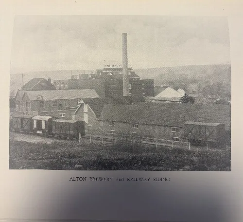 Old brewery buildings with a railway siding and train cars in front.