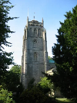 Stone church tower with gothic windows, surrounded by trees.