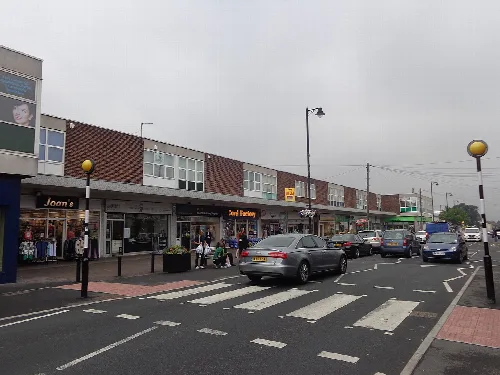 Ansicht von Geschäften, Fußgängern und parkenden Autos in Garforth.