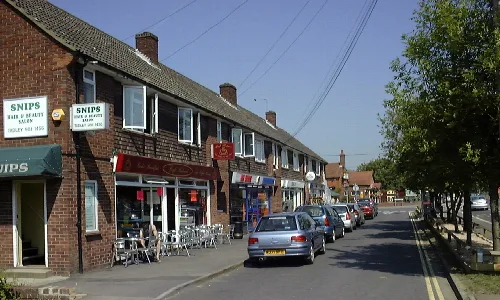 Shops on Mulfords Hill in Tadley with parked cars and outdoor seating.