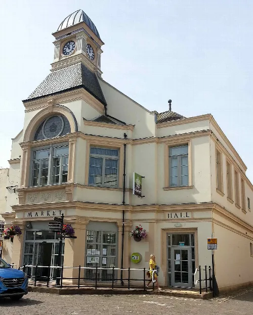 Ein cremefarbenes Gebäude mit Uhrturm und großen Fenstern, bezeichnet als Whitehaven Market Hall.