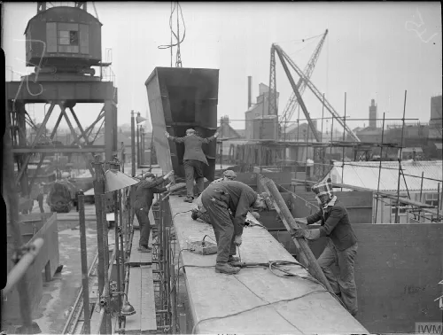 Men and a woman working on a ship at a shipyard with cranes and buildings in the background.