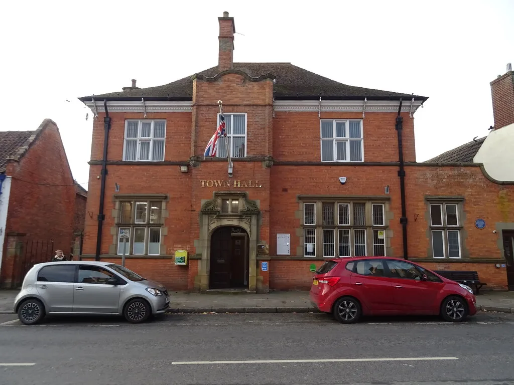 Red brick town hall with a Union Jack flag and parked cars in front.