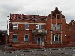 Rotes Backsteingebäude mit blauer Tür, mehreren Fenstern und dekorativen Giebeln.