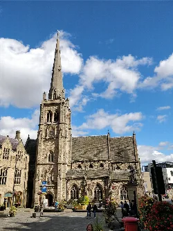 Stone church with tall spire and people in the square.