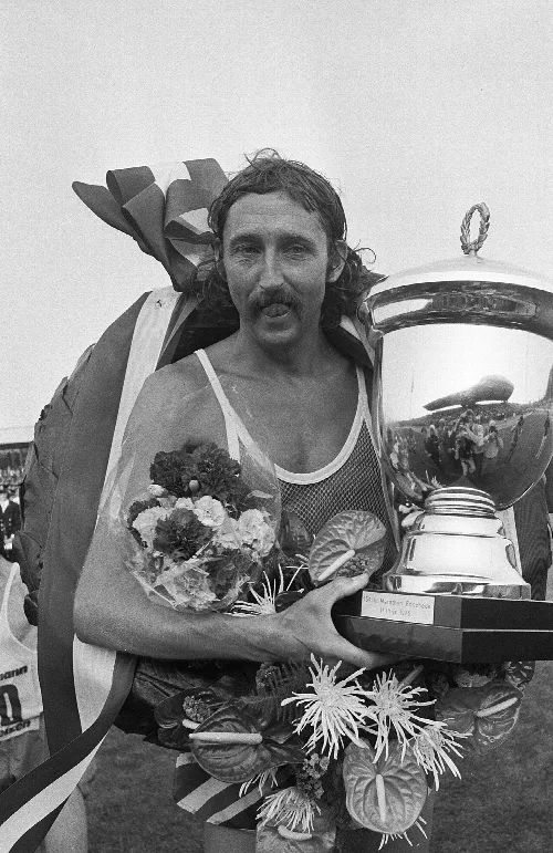 Ron Hill hält einen großen Pokal und Blumen, feiert seinen Sieg 1975.