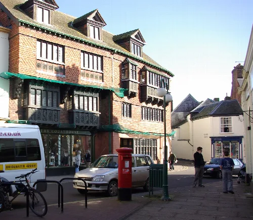 Casas de ladrillo con toldos verdes y coches aparcados en Wiveliscombe.