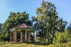 A small pavilion with a tiled roof and wooden columns in a green park.