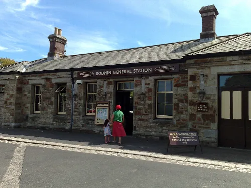 Stone railway station building with a sign and two people outside.