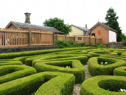 Jardín con topiarios y una caseta de madera en el fondo.