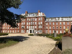 Red-brick college building with multiple windows and a curved pathway in front.