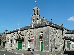 Edificio de piedra con puertas verdes, torre del reloj y cestas de flores en Cowbridge.