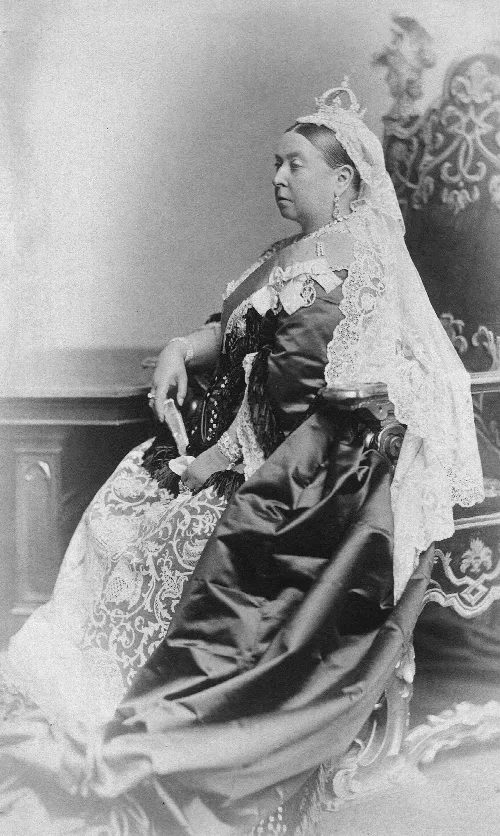 Queen Victoria in elaborate attire with lace and jewelry, seated in a chair.