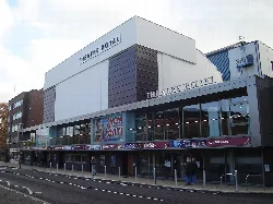 Edificio de teatro moderno con grandes ventanales de cristal y cartelera.