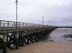 Muelle de madera con farolas en Amble, playa de arena en primer plano.