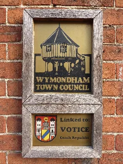 Placa en una pared de ladrillos que muestra la conexión del Ayuntamiento de Wymondham con Votice.