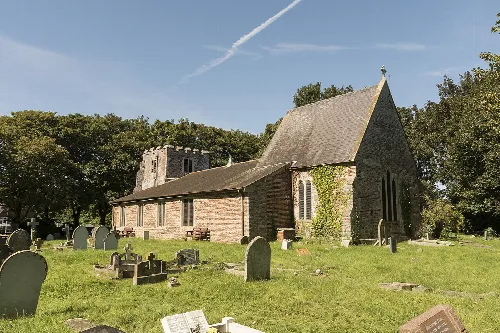 Stone church with graveyard and trees behind.
