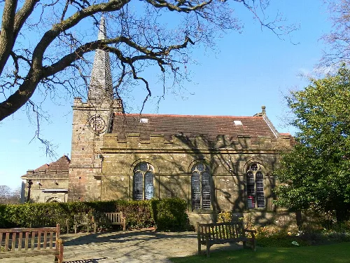 View of All Saints' church from the south, with benches and trees in front.