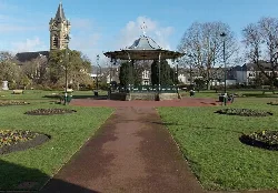 Quiosco octagonal en Victoria Gardens, Neath, con una torre de iglesia al fondo.