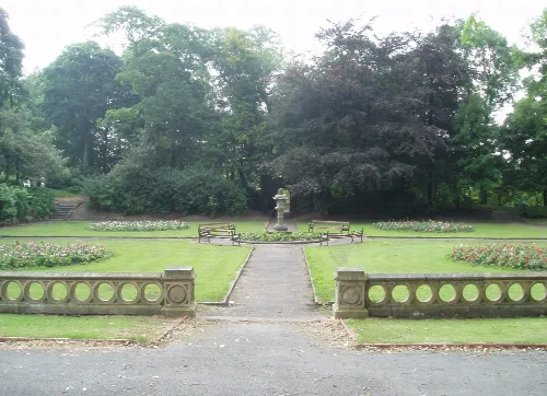 Ein Park mit Brunnen, Blumenbeeten, Bänken und Bäumen.