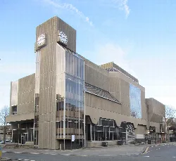 Ayuntamiento de hormigón con relojes en la parte superior y grandes ventanas de cristal en la esquina.