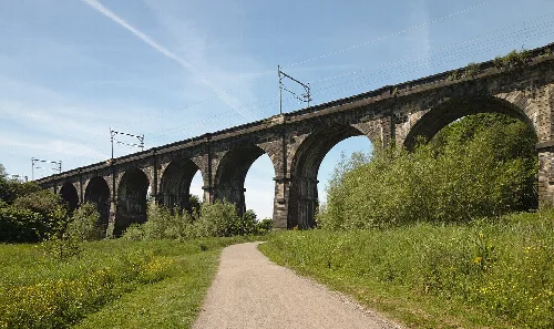 Ein steinerner Viadukt mit mehreren Bögen, gesehen von unten, mit Grünflächen und einem Weg im Vordergrund.