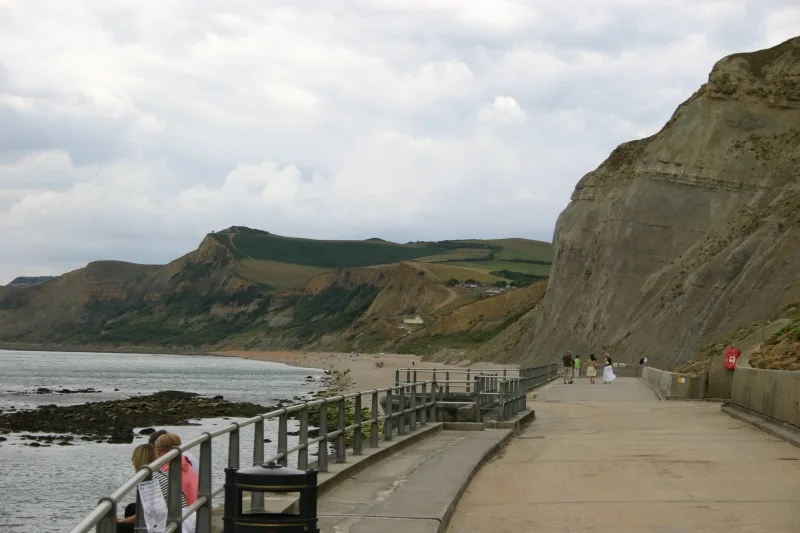Acantilados y paseo en West Bay, Dorset, con personas caminando y sentadas.