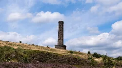 Ein hoher steinerner Turm auf einem grasbewachsenen Hügel mit Heide in Ramsbottom.